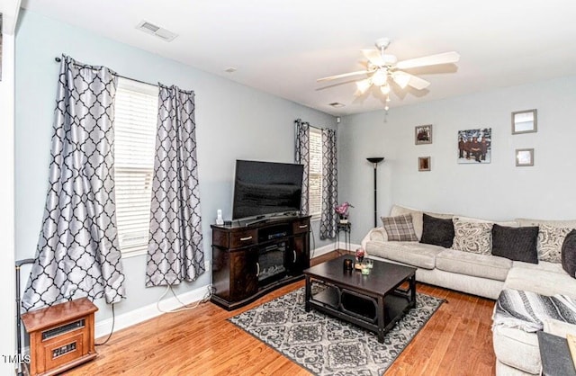 living room with a wealth of natural light, visible vents, a ceiling fan, and wood finished floors