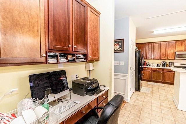 kitchen featuring light countertops, freestanding refrigerator, stainless steel range with electric stovetop, wainscoting, and brown cabinets