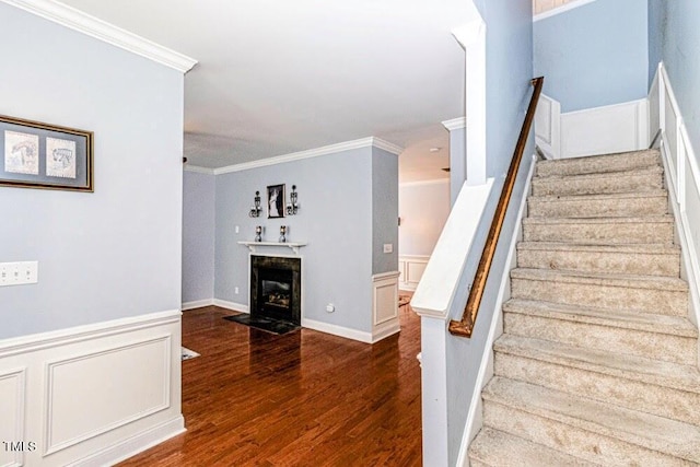 stairs with crown molding, a wainscoted wall, a fireplace with flush hearth, a decorative wall, and wood finished floors