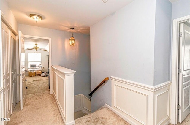 corridor featuring a decorative wall, light colored carpet, wainscoting, and an upstairs landing