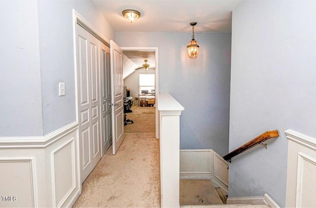 corridor with a decorative wall, wainscoting, and light colored carpet