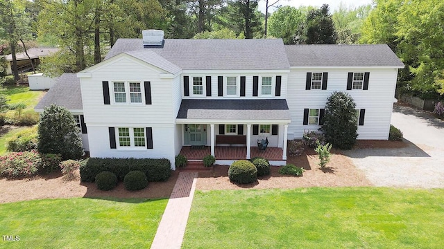 view of front of property with a porch, roof with shingles, a chimney, and a front lawn