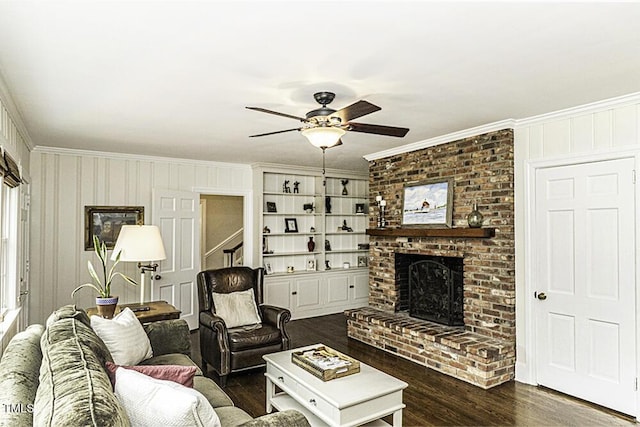 living room with crown molding, a ceiling fan, stairs, a brick fireplace, and dark wood finished floors