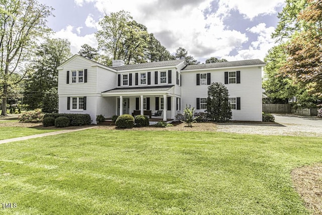 traditional-style home featuring a front yard, fence, and covered porch