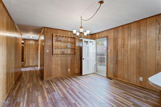 unfurnished dining area with an inviting chandelier, dark wood-style flooring, wooden walls, and visible vents