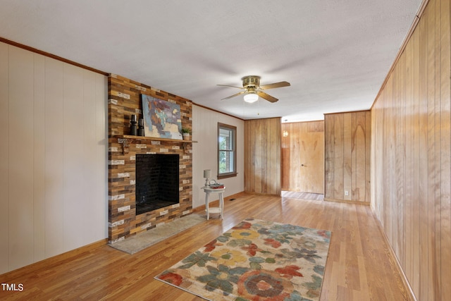 unfurnished living room featuring ornamental molding, ceiling fan, wooden walls, and hardwood / wood-style floors