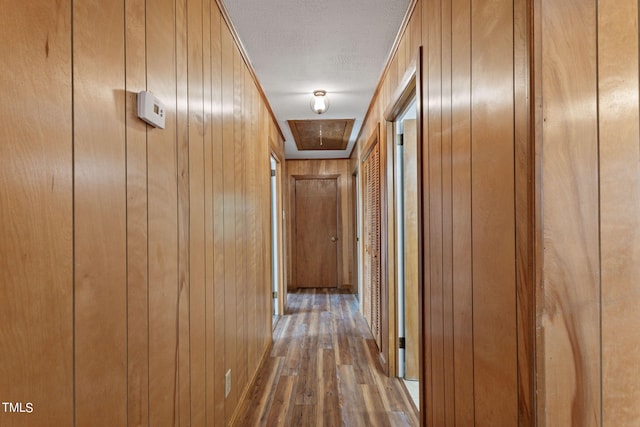 corridor with a textured ceiling, wood finished floors, and wooden walls