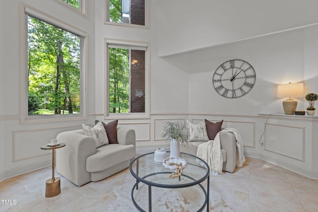 living area with light tile patterned flooring, a decorative wall, and a wainscoted wall