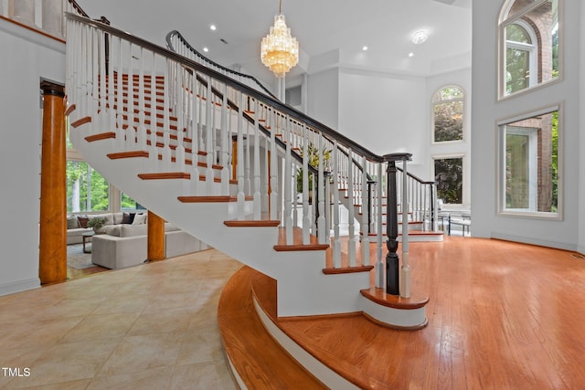 staircase featuring a towering ceiling, a notable chandelier, baseboards, and a healthy amount of sunlight