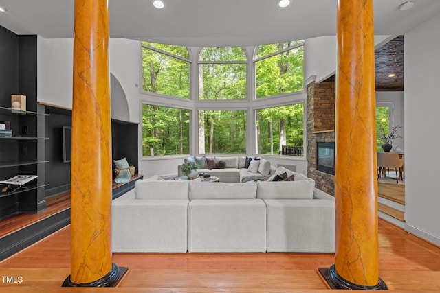 living room featuring ornate columns, wood finished floors, recessed lighting, and a stone fireplace