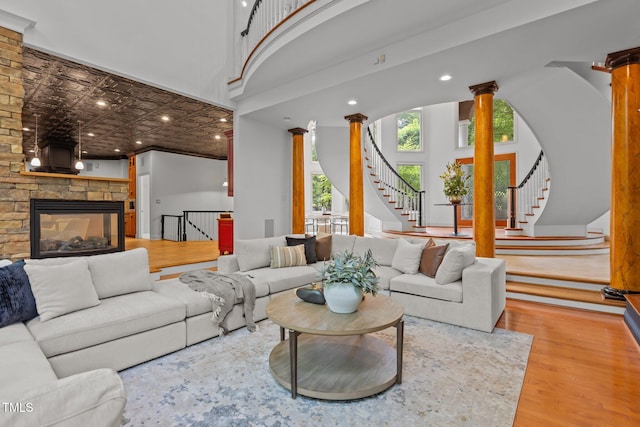 living room featuring recessed lighting, stairway, a stone fireplace, ornate columns, and wood finished floors