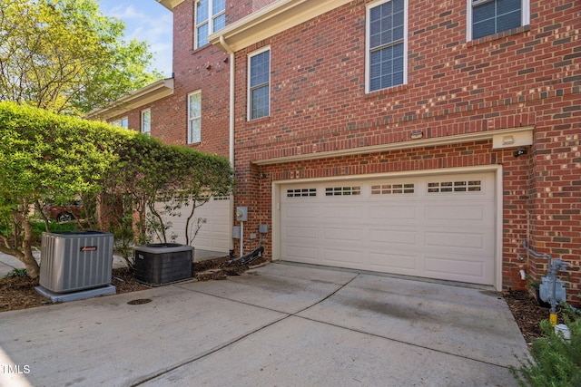 view of side of property with concrete driveway, brick siding, a garage, and central air condition unit