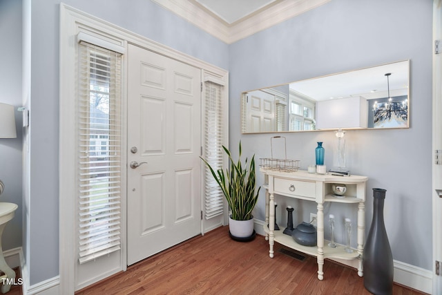 entrance foyer with a chandelier, baseboards, crown molding, and wood finished floors