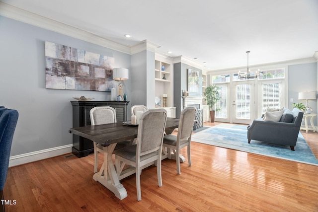 dining area featuring a fireplace with flush hearth, a notable chandelier, crown molding, and light wood finished floors