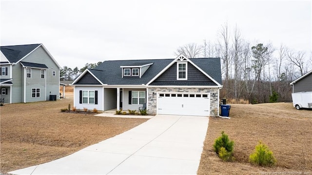 craftsman-style house with central AC unit, driveway, and stone siding