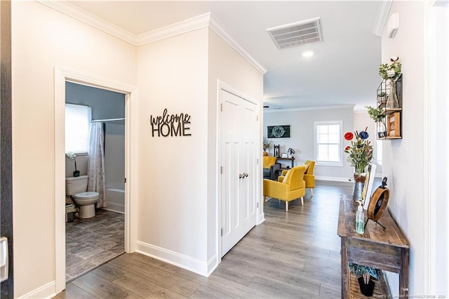 corridor with light wood-style flooring, baseboards, ornamental molding, and visible vents