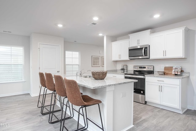2134 Monk Dr, Haw River, NC 27258 - kitchen featuring stainless steel appliances, an island with sink, a breakfast bar, white cabinets, and light wood-style floors