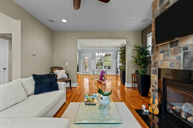 living room featuring ceiling fan with notable chandelier, a fireplace, crown molding, light wood-type flooring, and baseboards