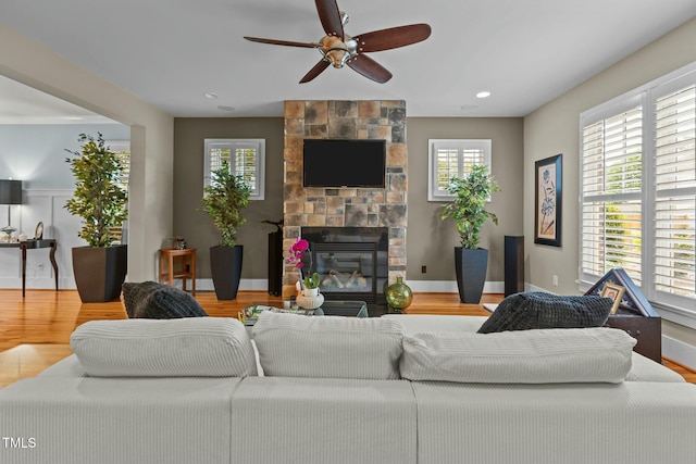 living room with a stone fireplace, a healthy amount of sunlight, wood finished floors, and ceiling fan
