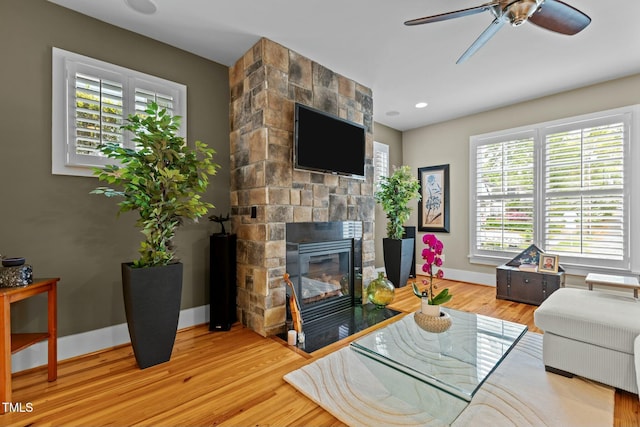 living room featuring wood finished floors, recessed lighting, a ceiling fan, baseboards, and a stone fireplace