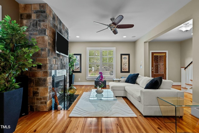 living area featuring baseboards, a stone fireplace, ceiling fan, wood finished floors, and stairway