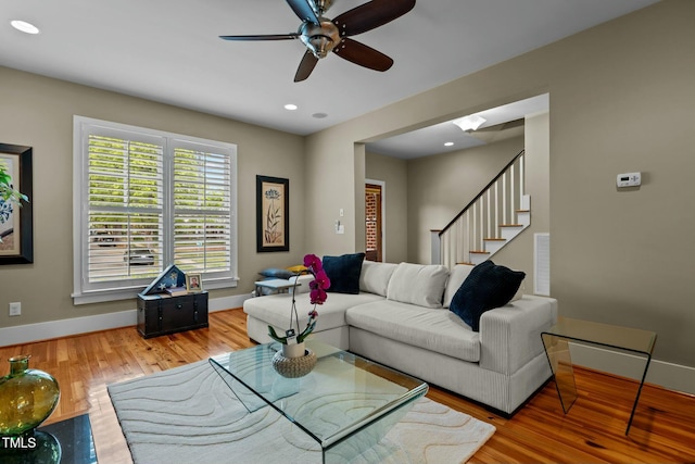 living area with wood finished floors, a ceiling fan, visible vents, baseboards, and stairway