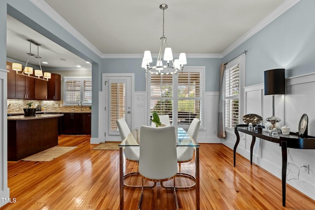 dining area with ornamental molding, wainscoting, a chandelier, a decorative wall, and light wood-style floors