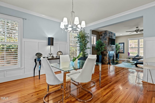 dining space with wood finished floors, a wainscoted wall, a fireplace, a decorative wall, and ornamental molding