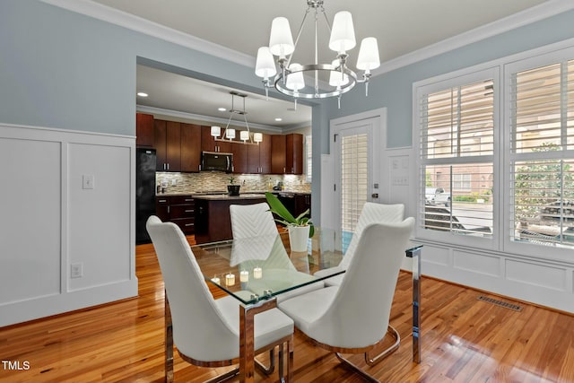dining room with an inviting chandelier, a wainscoted wall, light wood-type flooring, a decorative wall, and ornamental molding