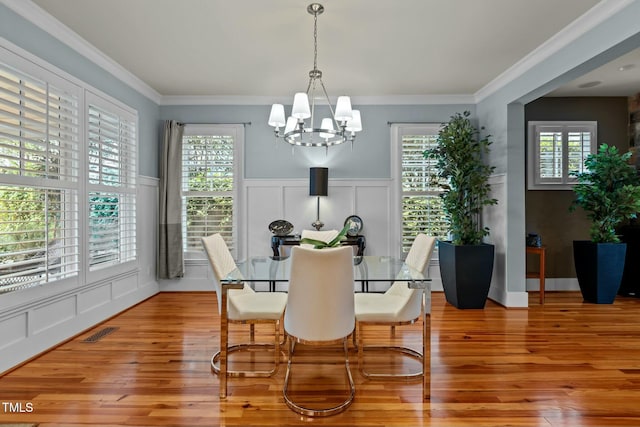 dining space featuring a notable chandelier, light wood-style flooring, visible vents, a decorative wall, and crown molding