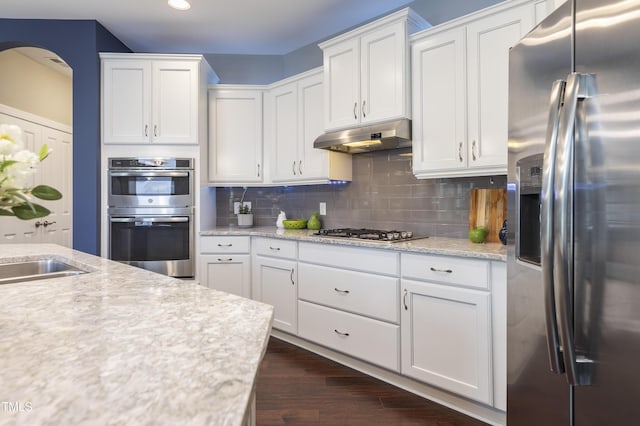 1005 Vesper Ct, Durham, NC 27703 - kitchen with appliances with stainless steel finishes, under cabinet range hood, arched walkways, white cabinetry, and dark wood finished floors