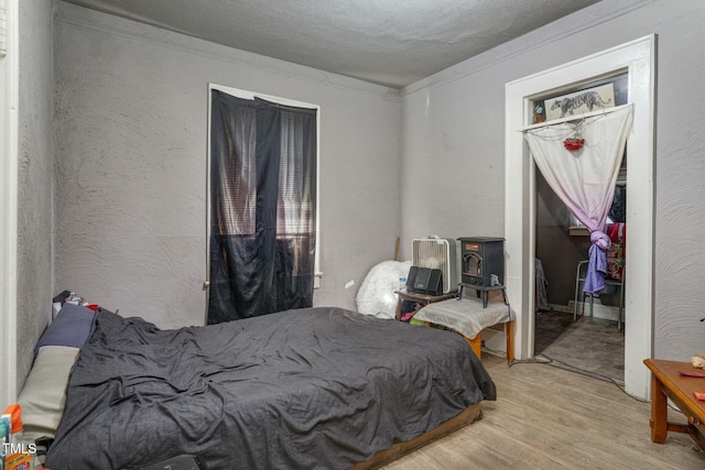 bedroom featuring a textured ceiling, wood finished floors, a textured wall, and ornamental molding