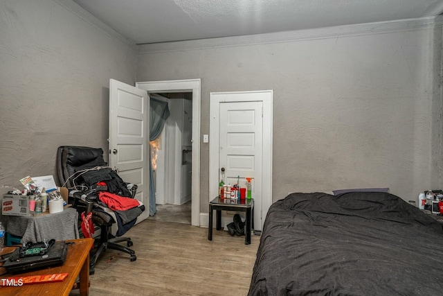 bedroom with a textured wall, crown molding, and wood finished floors