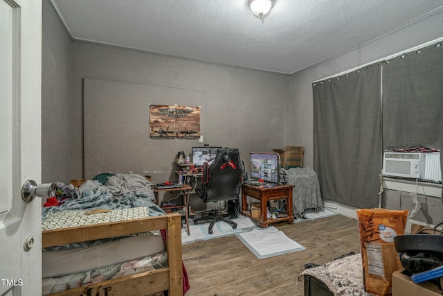 bedroom featuring a textured wall, cooling unit, a textured ceiling, and wood finished floors