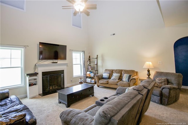 living area with a towering ceiling, light carpet, a fireplace, visible vents, and ceiling fan