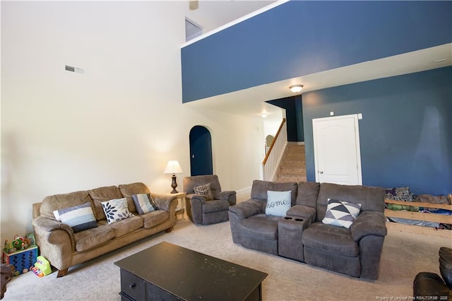 carpeted living area featuring a high ceiling, visible vents, and stairway