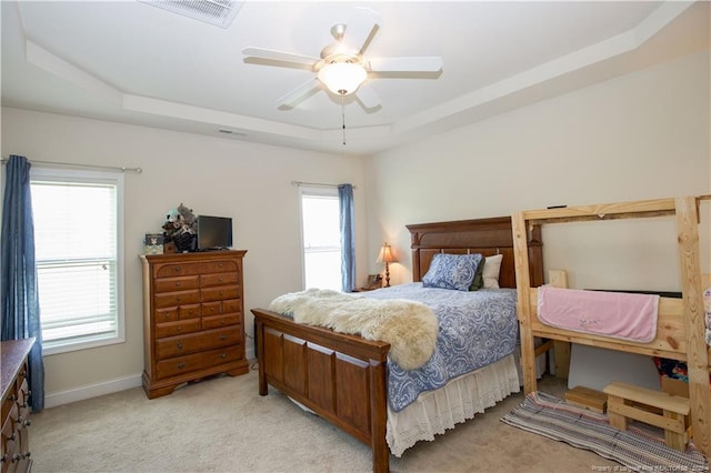 bedroom featuring visible vents, baseboards, a raised ceiling, a ceiling fan, and light carpet