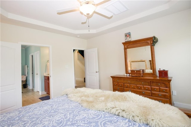 bedroom featuring ensuite bathroom, a tray ceiling, baseboards, and ceiling fan