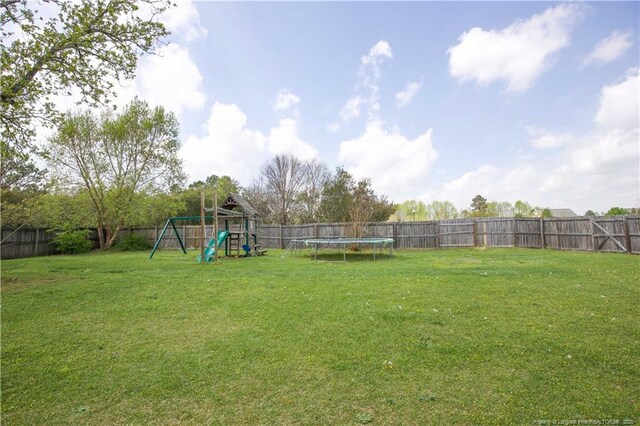 view of yard with a trampoline, a fenced backyard, and a playground