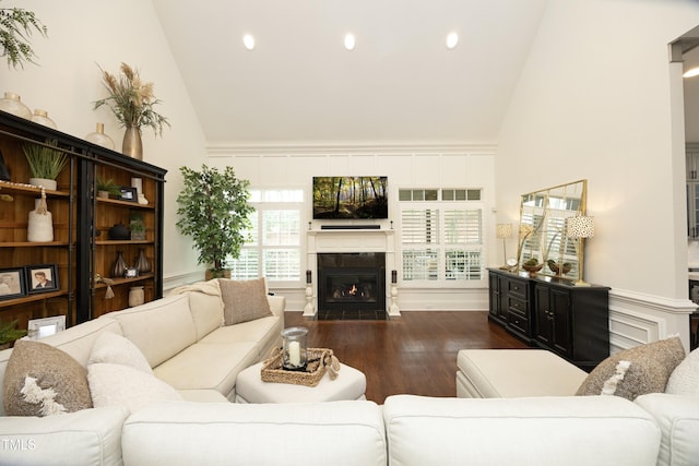 living area with a decorative wall, high vaulted ceiling, a fireplace with flush hearth, recessed lighting, and wood finished floors