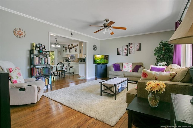 living area with crown molding, wood finished floors, and ceiling fan with notable chandelier