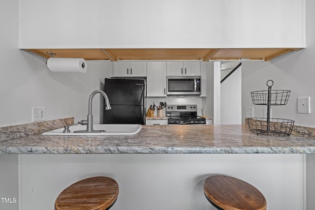 kitchen featuring light stone counters, a peninsula, white cabinets, stainless steel appliances, and a sink