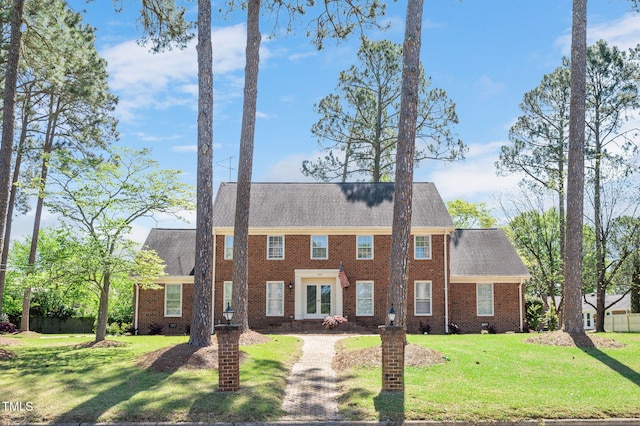 colonial inspired home featuring a shingled roof, brick siding, and a front lawn