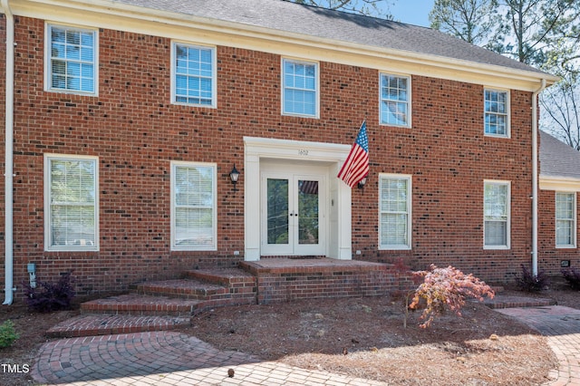 view of front of house featuring roof with shingles, brick siding, and french doors