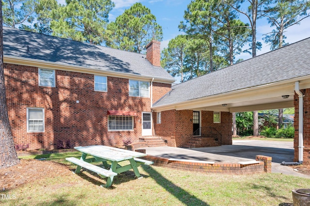 rear view of house featuring a yard, entry steps, roof with shingles, brick siding, and a chimney
