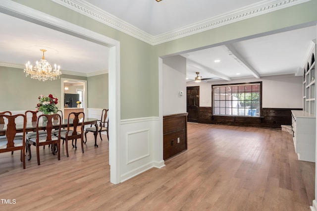 interior space with wainscoting, ceiling fan with notable chandelier, crown molding, and light wood-style flooring