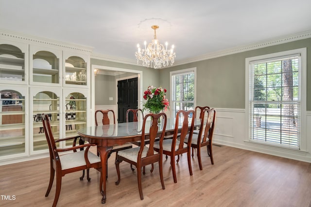 dining area with a decorative wall, an inviting chandelier, light wood-style flooring, ornamental molding, and wainscoting