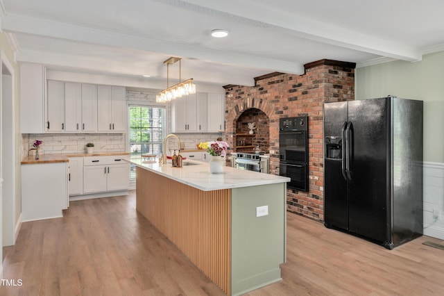 kitchen featuring light wood-style flooring, black appliances, beam ceiling, decorative backsplash, and a sink
