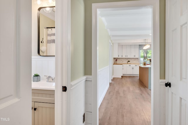 hallway with a sink, ornamental molding, a decorative wall, light wood finished floors, and wainscoting