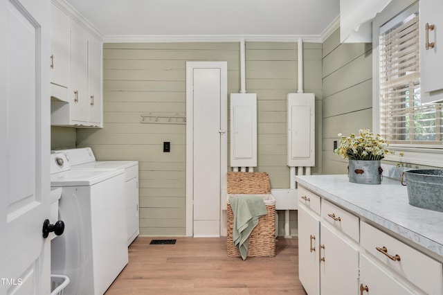 clothes washing area with electric panel, crown molding, cabinet space, light wood-style flooring, and washing machine and dryer